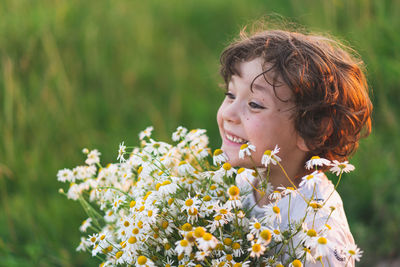 Cute smiling boy at camomile field at sunset in soft sunlight. boy and daisies.