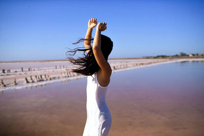 Woman in white dress with long dark hair in wind on beach of pink sea.