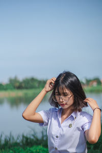 Woman standing by lake against clear blue sky