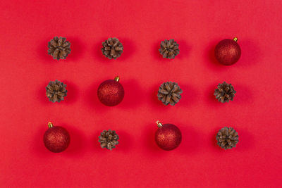 High angle view of christmas baubles and pine cones against red background