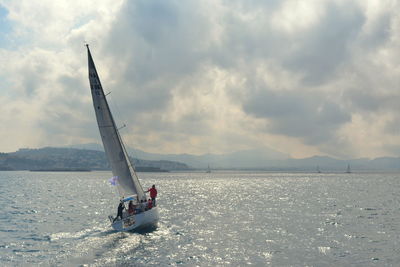 People on sailboat sailing in sea against sky