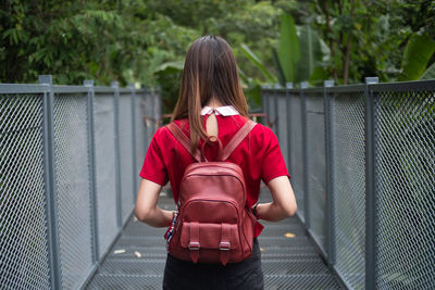 Rear view of woman with backpack standing on footbridge in forest