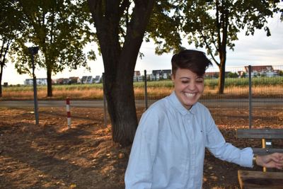 Portrait of smiling man standing by tree against sky