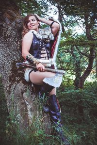 Portrait of smiling young woman standing on tree trunk in forest