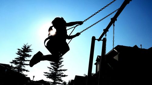 Low angle view of silhouette girl swinging against clear blue sky