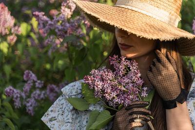 Attractive  young woman in retro boatman's straw hat in a lilac blooming garden. touches her hair.