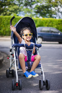 Full length of girl waving hand while sitting on baby stroller at street