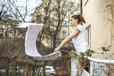 Side view of woman dusting carpet while standing in balcony