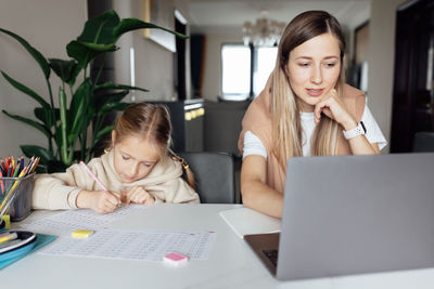 Mother working on laptop while daughter doing homework