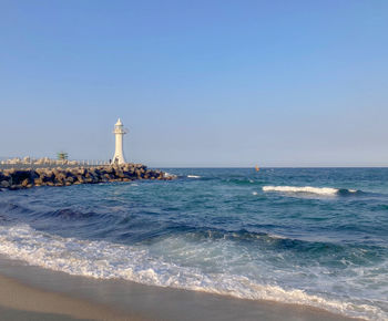 Lighthouse by sea against clear sky