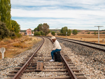 Side view of woman with luggage sitting on railroad track