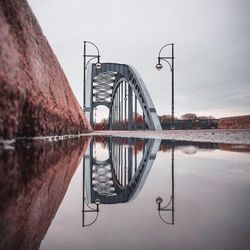Reflection of bridge on puddle against cloudy sky