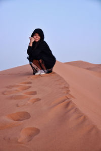 Woman crouching at desert against clear sky