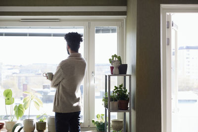 Man holding coffee mug and looking through window