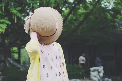 Woman covering face with hat against trees in forest