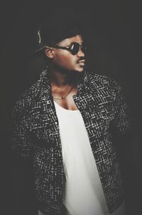 Young man wearing sunglasses standing against black background