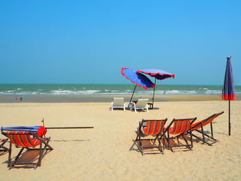 Deck chairs and parasols at beach against clear sky