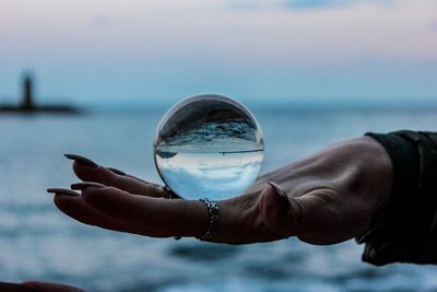 Close-up of hand holding crystal ball against sea