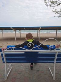 Rear view of man sitting on chair at beach against sky