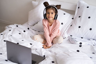 Portrait of girl listening music while sitting on bed