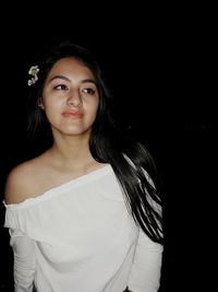 Portrait of young woman standing against black background