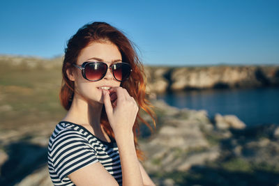 Portrait of woman wearing sunglasses at beach against sky