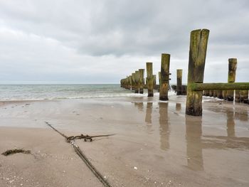 Wooden posts on beach against sky