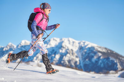 Low angle view of man skiing on snowcapped mountain against clear blue sky