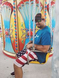 Young man wearing sunglasses sitting on carousel