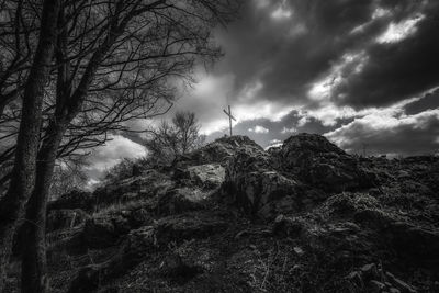 Low angle view of cross on rock formation against cloudy sky