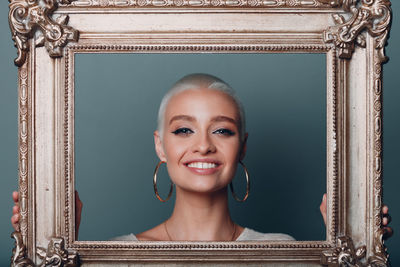 Portrait of young woman with picture frame against colored background