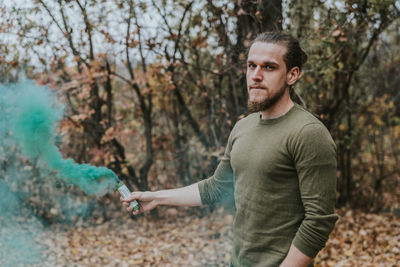 Portrait of young man standing by tree in forest