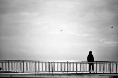 Rear view of man standing on railing against sky