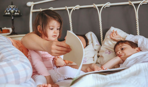 Close-up of mother telling bed time story to children on bed at home