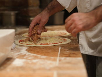 Midsection of chef preparing pizza at table in kitchen