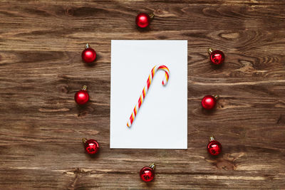 Striped lollipop on a blank sheet of paper and and red christmas balls on a wooden background. 