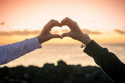 Cropped image of people making heart shape against sky during sunset