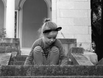 Girl crouching on staircase against entrance of house