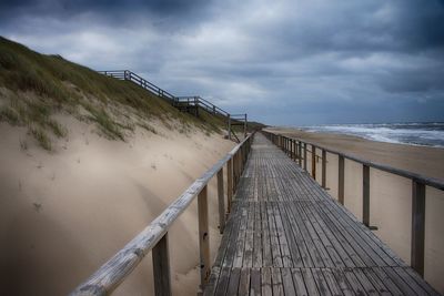 Wooden pier on beach against sky