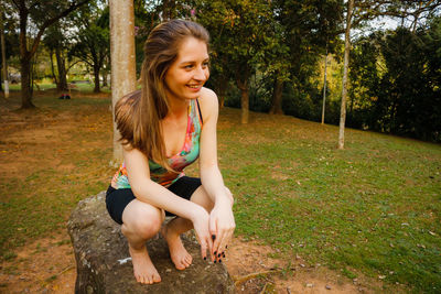 Smiling young woman crouching on rock at park