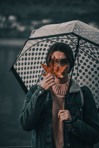 Portrait of teenage girl holding umbrella and maple leaf while standing outdoors