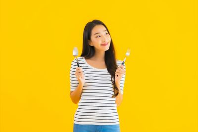 Portrait of smiling young woman against yellow background