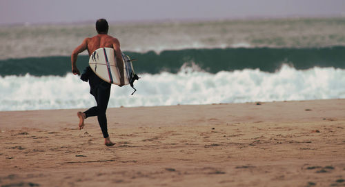 Rear view of man with surfboard running at beach