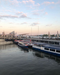 Boats moored in river against sky during sunset