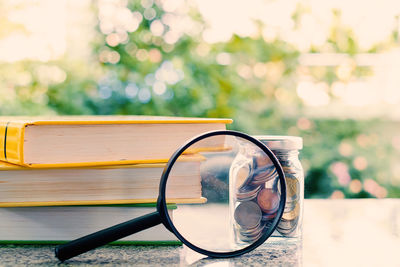 Coins in jar with magnifying glass and book on table