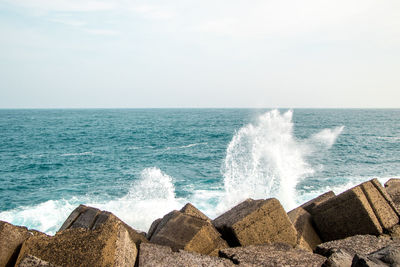 Waves splashing on rocks by sea against sky