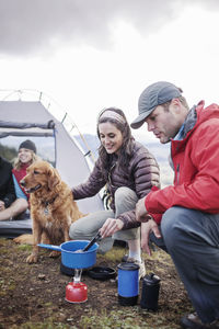 Friends preparing food by dog at campsite