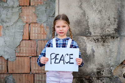 Portrait of cute girl holding poster against wall