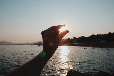 Hand holding sea against sky during sunset