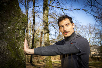 Young man is doing stretching in the woods while he is listening to the music.